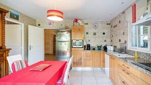 A kitchen with wooden cabinets, a stainless steel refrigerator, a microwave, and a red dining table.