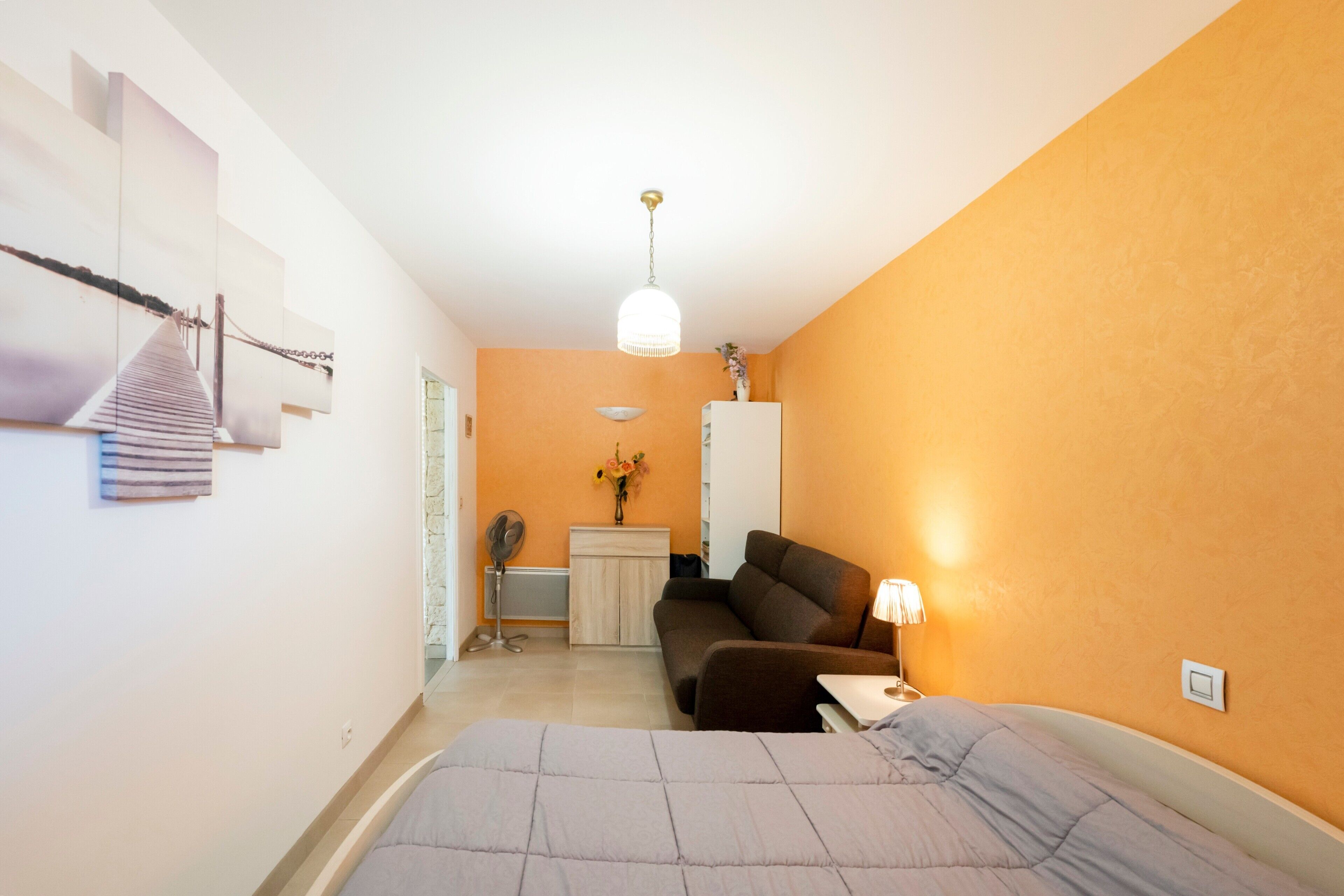 Un dormitorio con cama, escritorio, sillón, sofá y lámpara colgante.