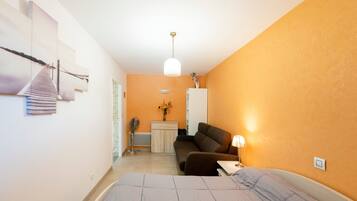 Un dormitorio con cama, escritorio, sillón, sofá y lámpara colgante.