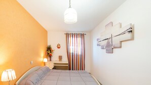 A bedroom with a bed, bedside table, lamp, dresser, and a window with curtains.