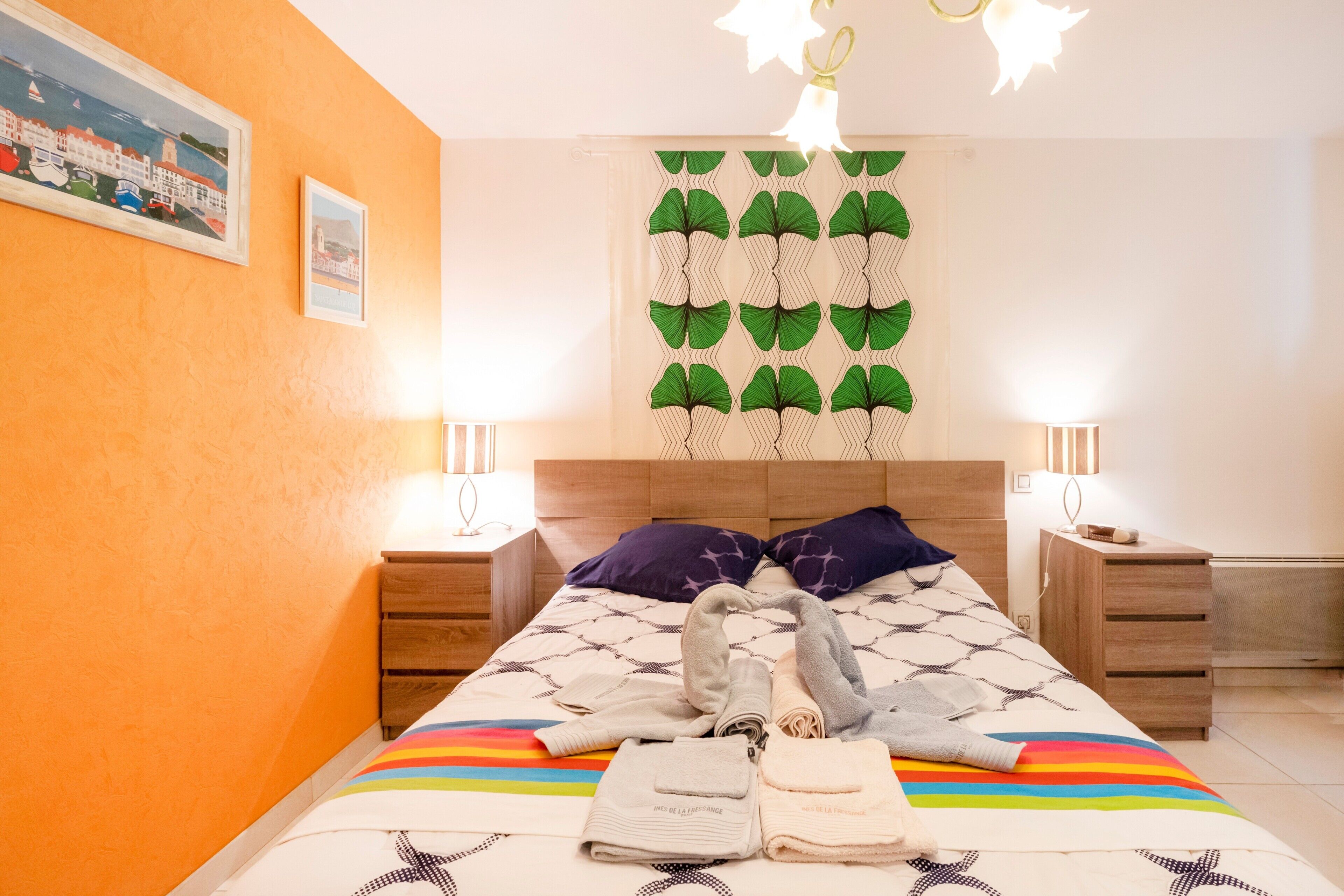 Ein Schlafzimmer mit einem Bett, zwei Nachttischen, einer Kopfteil und einer Wand mit einem gemusterten Vorhang.