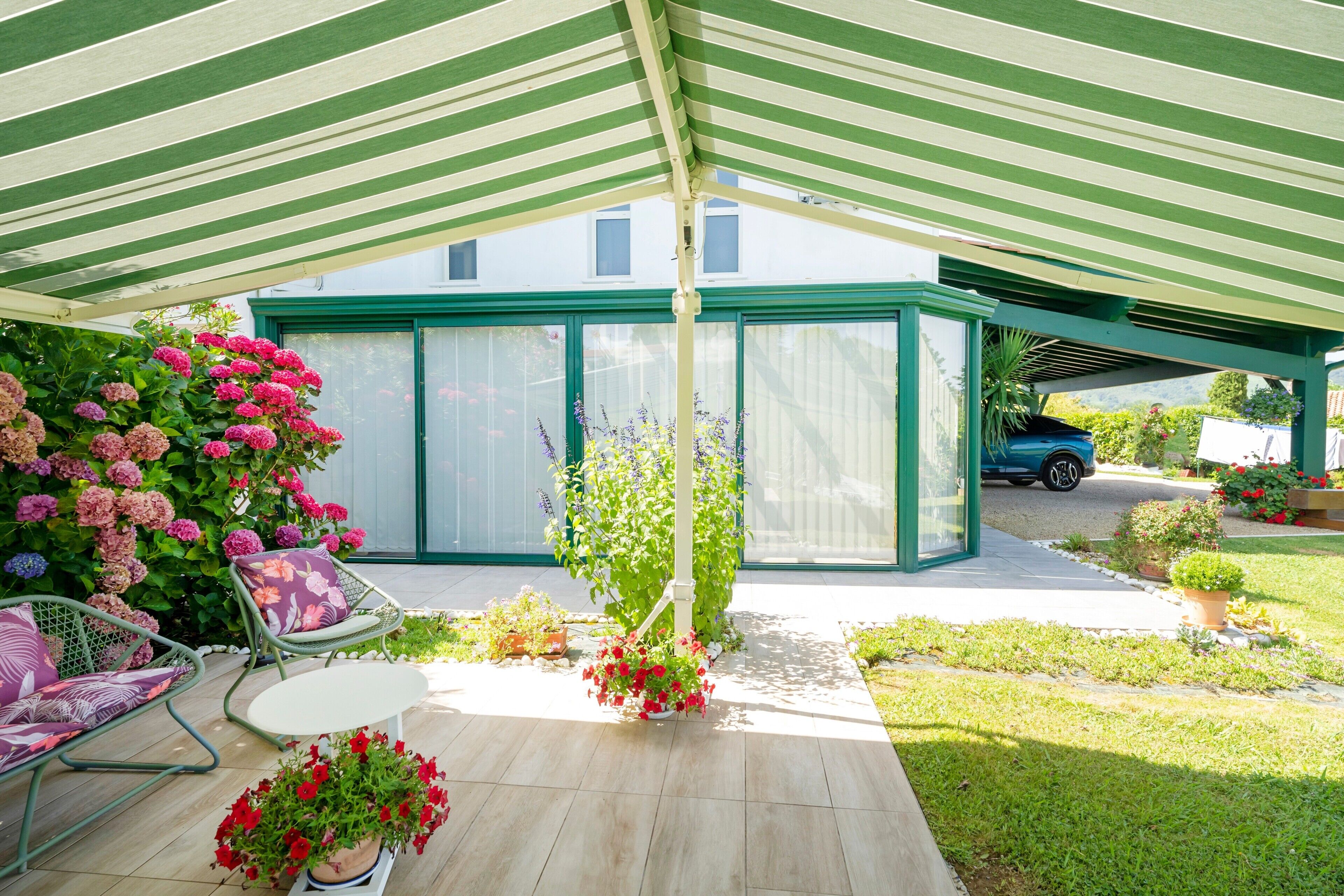 Een overdekt terras met een groen en wit gestreept dak, een glazen omheining met groene lijst en een zithoek met een witte tafel en stoelen.