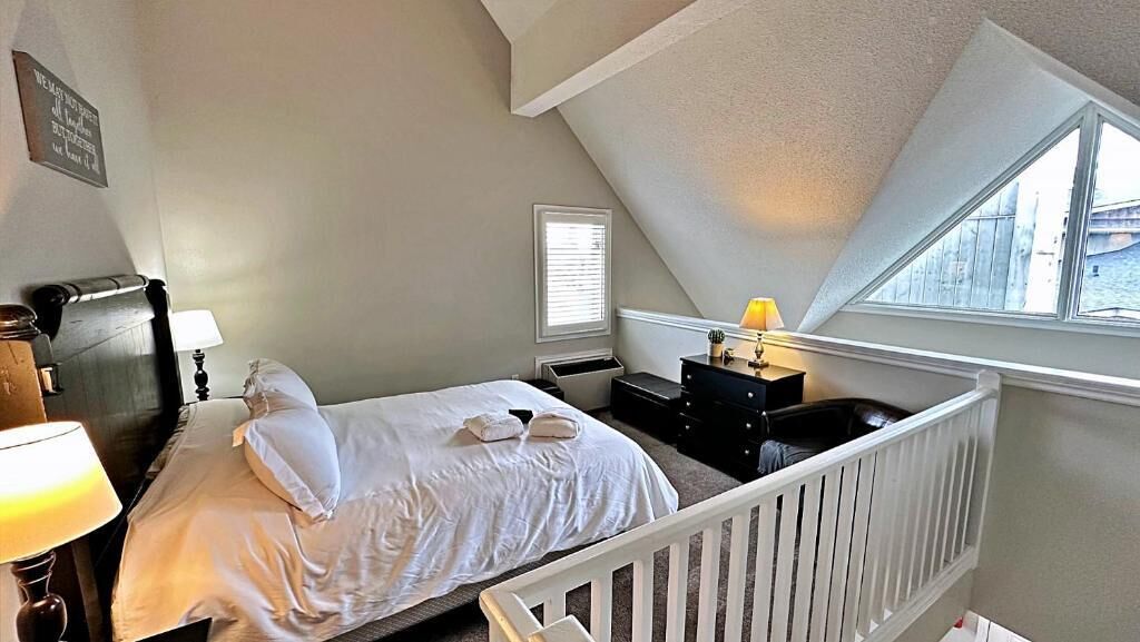 A bedroom with a bed, a nightstand, a dresser, a window, and a crib.