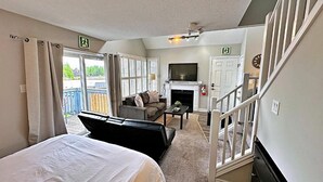 Hotelkamer met een bed, een bank, een televisie, een open haard en een balkon met uitzicht op bomen.