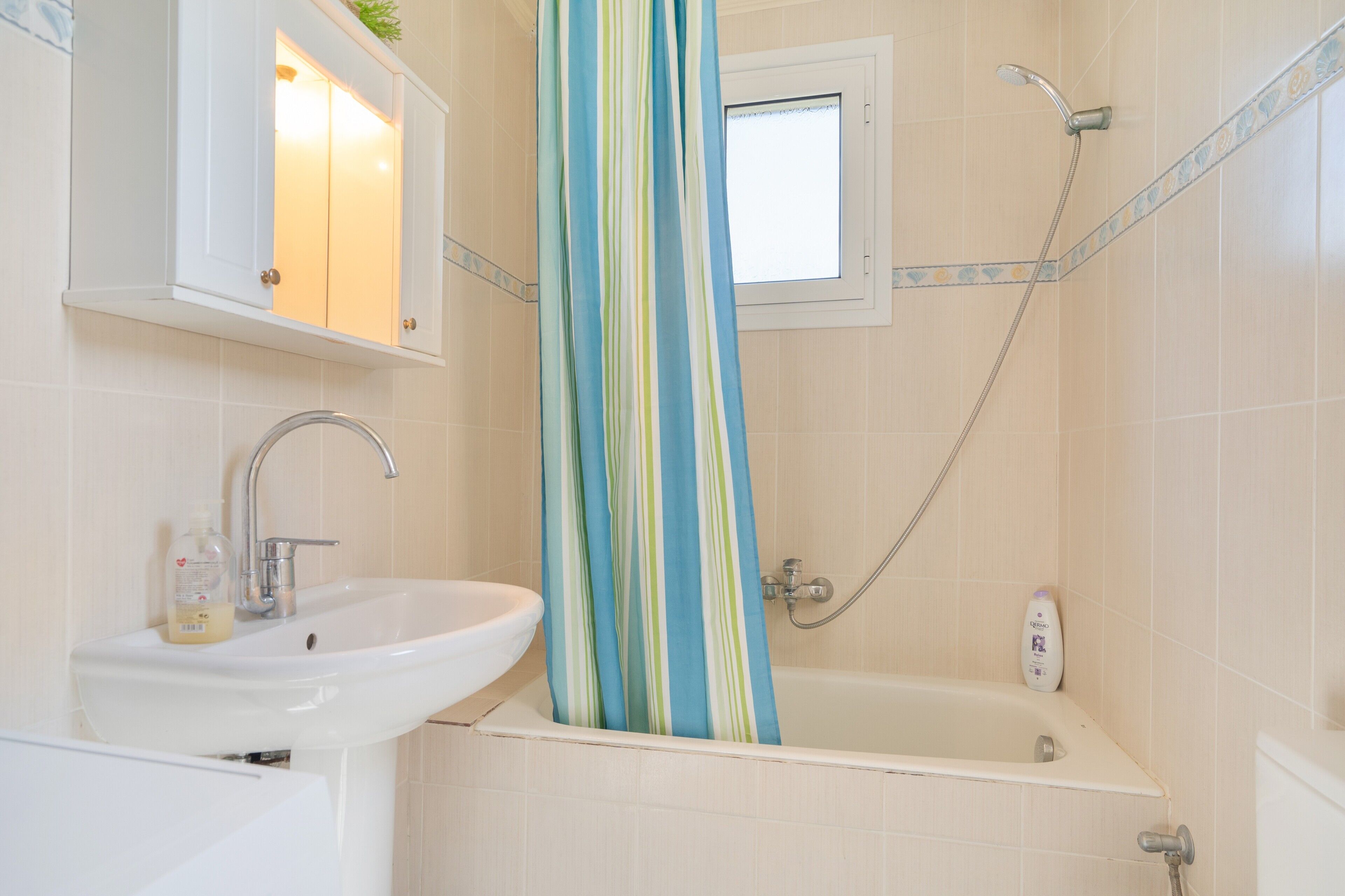 Une salle de bain avec un lavabo, un miroir, une douche et une fenêtre.
