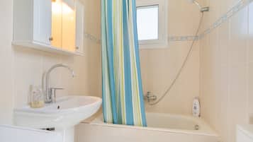 Une salle de bain avec un lavabo, un miroir, une douche et une fenêtre.