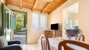 A room with a wooden ceiling, a dining table with chairs, a television, and a potted plant.
