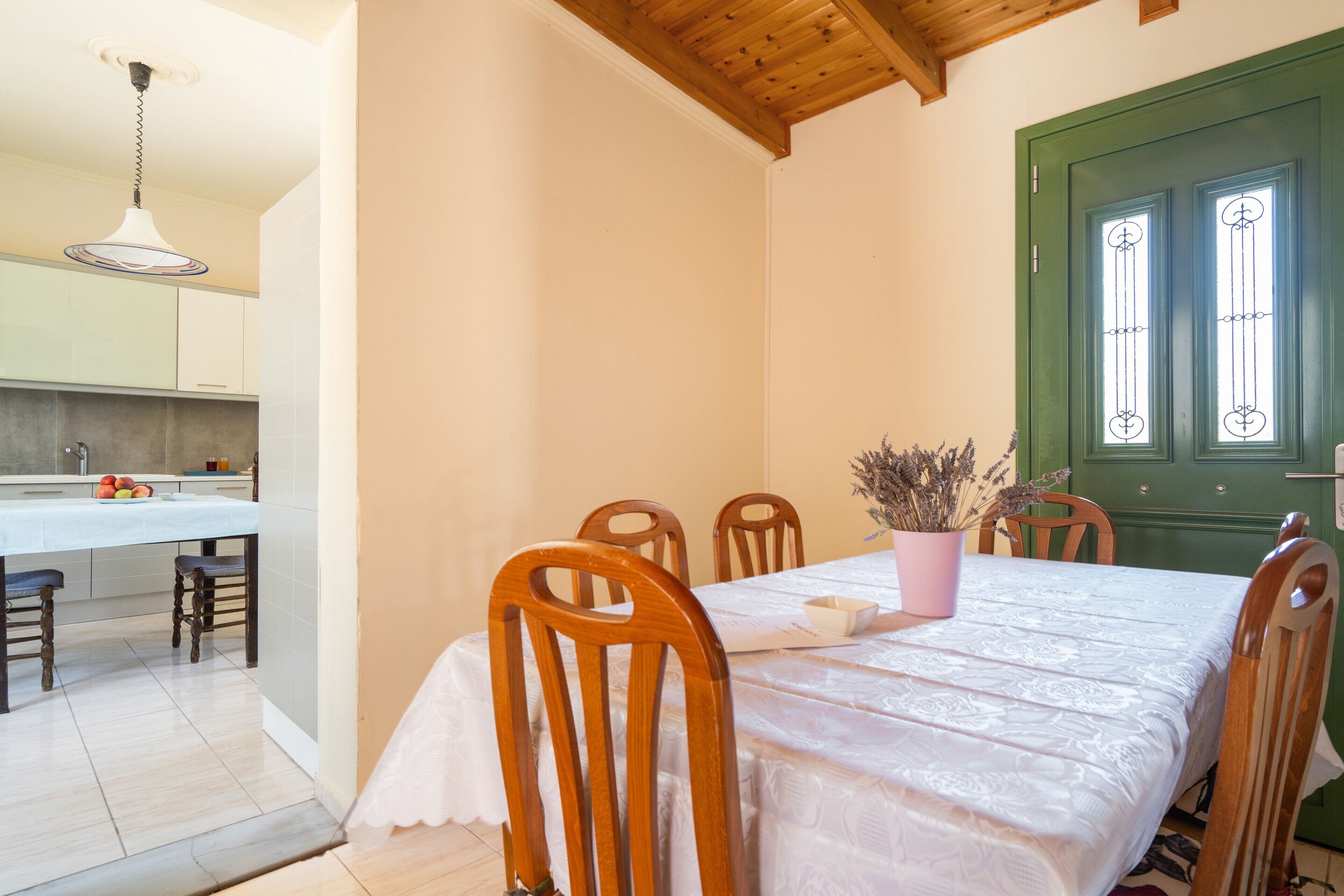 Un comedor con una mesa dispuesta para cuatro, sillas de madera, mantel blanco y una puerta verde con ventanas.