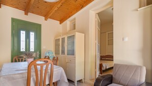 A room with a wooden ceiling, a green door, a white cabinet, a bed, and a chair.