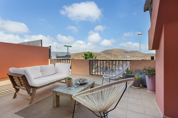 A balcony with a sofa, chairs, a table, and potted plants.