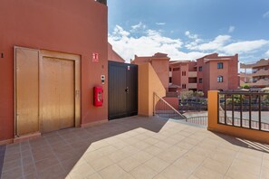 Ein Gebäudeeingang mit zwei Türen, einem Feuerlöscher und einem befestigten Bereich, der in einen Innenhof führt.