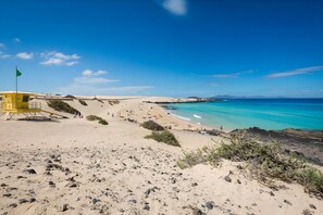 A beach with a lifeguard tower, clear turquoise waters, and sandy dunes.