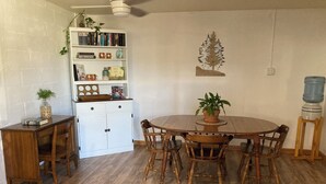 A dining area with a wooden table and chairs, a bookshelf with books and decorative items, and a water dispenser.