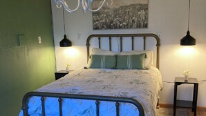 A bedroom with a bed, a bench, a chandelier, two bedside tables, and a painting on the wall.