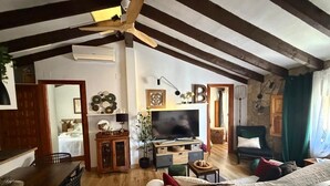 A spacious living room with exposed wooden beams, a television, a sofa, and a dining area with a table and chairs. - Casa Trinidad – private terrace, parking, historic center of Dénia (Dénia)