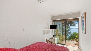 A bedroom with a bed, a television, a chair, and a view of the outdoors. - Room 'Bagaud' with Sea View, Shared Terrace and Wi-Fi (La Croix-Valmer)