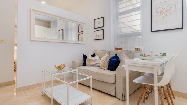 Un salon moderne avec un canapé, une table basse en verre, une table à manger avec des chaises et des œuvres d’art encadrées accrochées aux murs.