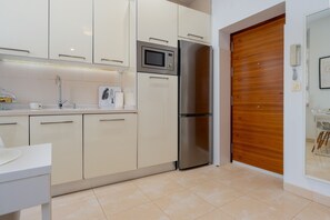 A modern kitchen with white cabinets, a stainless steel refrigerator, a microwave, and a wooden door. - Apartment 'Alameda Cool' with Wi-Fi and Air Conditioning (Sevilla)