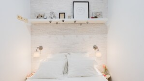 Un lit avec une literie blanche, deux lampes fixées au mur, une étagère avec des objets décoratifs et un mur dont le motif rappelle celui d’un mur de briques.