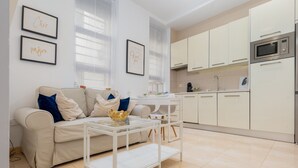 Un salon moderne avec un canapé, une table basse en verre et un coin cuisine équipé de placards et d’un four à micro-ondes.
