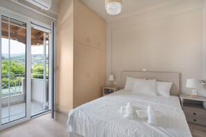 Un dormitorio con una cama grande, un ventanal corredero a un balcón y vistas al verdor.