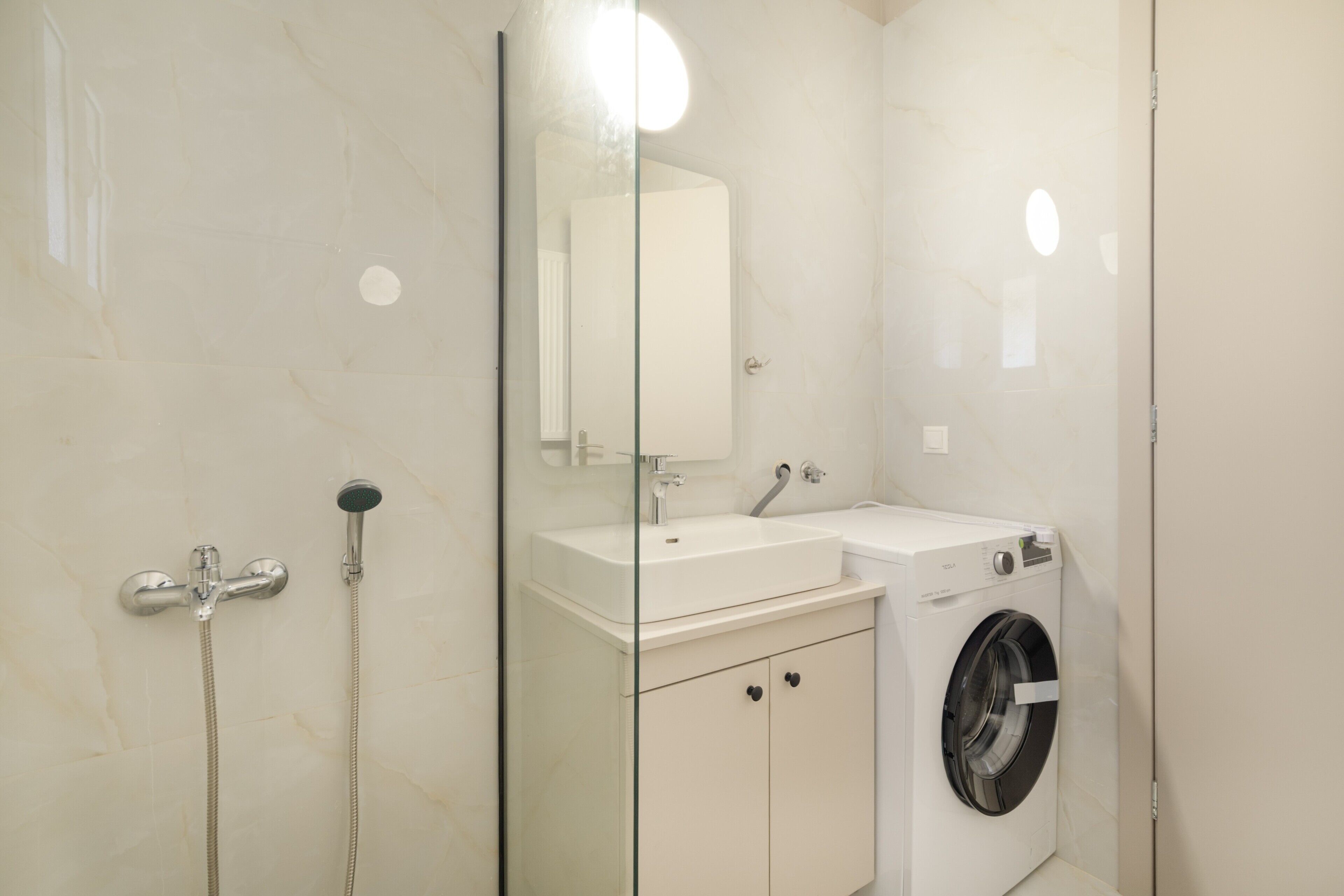 Un baño con cabina de ducha de vidrio, lavamanos, espejo y lavadora.