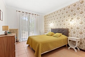 A bedroom with a bed, a bedside table, a lamp, a radiator, and a window with curtains.