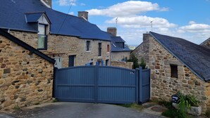 A stone house with a blue roof, a gated driveway, and a clear sky.
