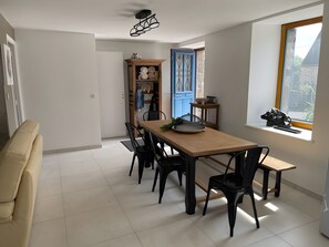 Un coin repas avec une table en bois, des chaises noires, une porte bleue et une fenêtre donnant sur un paysage.