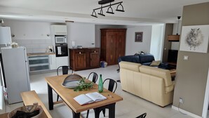 A modern kitchen with white cabinets, a wooden dining table, and a beige sofa in the living area.