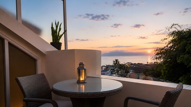 A round table with two wicker chairs, a potted plant, and a lit lantern on a balcony overlooking a sunset view. - Vacation 'Colina Blanca Sunset View' with Sea View, Shared Pool and Wi-Fi (Costa Adeje)