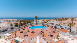 A rooftop pool with lounge chairs and umbrellas, surrounded by buildings with a view of the sea. - Vacation 'Colina Blanca Sunset View' with Sea View, Shared Pool and Wi-Fi (Costa Adeje)