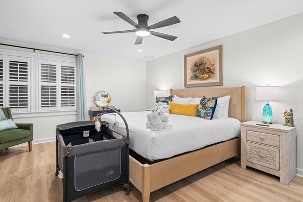A bedroom with a bed, a nightstand, a ceiling fan, a window with shutters, and a green chair.