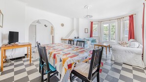 Een kamer met een eettafel, stoelen, een bank, een televisie en een trap.