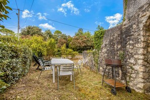 Une terrasse avec une table et des chaises, entourée de verdure et d’un mur de pierres.