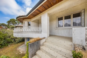A two-story building with a balcony, a set of stairs leading to the entrance, and a window with curtains. - Escapade au Lac – Comfortable House with Garden in Lacanau (Lacanau)