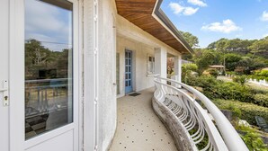 Een overdekt buitengebied met een witte balustrade, een blauwe deur en uitzicht op een tuin.