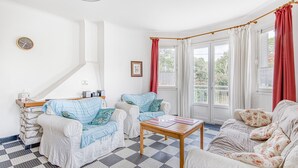 Een kamer met twee witte banken, een houten salontafel, een klok en een raam met gordijnen.