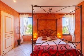 Ein Himmelbett mit roter Bettdecke, zwei Nachttischlampen und Blick auf Grünflächen außerhalb.