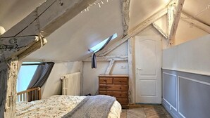 Un dormitorio con techo inclinado, un aparador de madera, una cama con colcha estampada y un radiador.