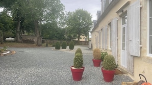 Un patio de grava con plantas topiarias en macetas, un leñedo y una carretilla.