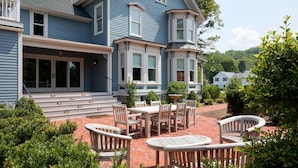 A two-story house with a covered patio area featuring a brick floor and wooden furniture.