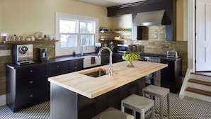 A modern kitchen with a central island, black cabinetry, a stainless steel range hood, and a checkered floor pattern.