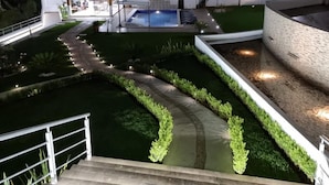 A modern outdoor area with a swimming pool, a covered seating area, and a well-lit pathway.