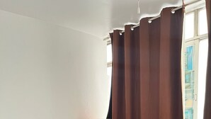 Une chambre à coucher avec un lit, une table de chevet en bois, une fenêtre avec des rideaux et une vue sur les bâtiments à l’extérieur.