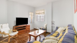 A living room with a TV, wooden furniture, a sofa, and a window with curtains. - Holiday Home 'El Atico' with Sea Views, Private Terrace and Wi-Fi (Las Palmas)