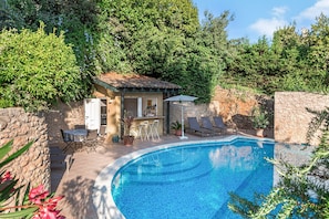 Una piscina amb gandules, una petita zona de bar i una paret de pedra.