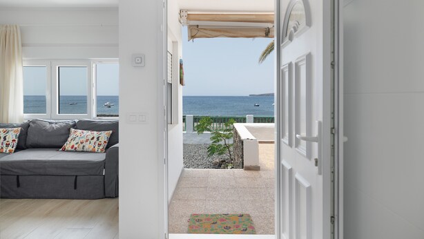 A room with a grey sofa, a view of the sea, and a balcony with a white door.