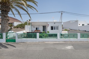 Un edificio blanco con cerca verde, una palmera y cielo despejado.