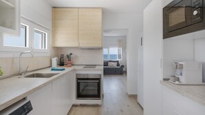 A modern kitchen with a dishwasher, oven, and microwave. There is a window providing natural light and a view of the living area.